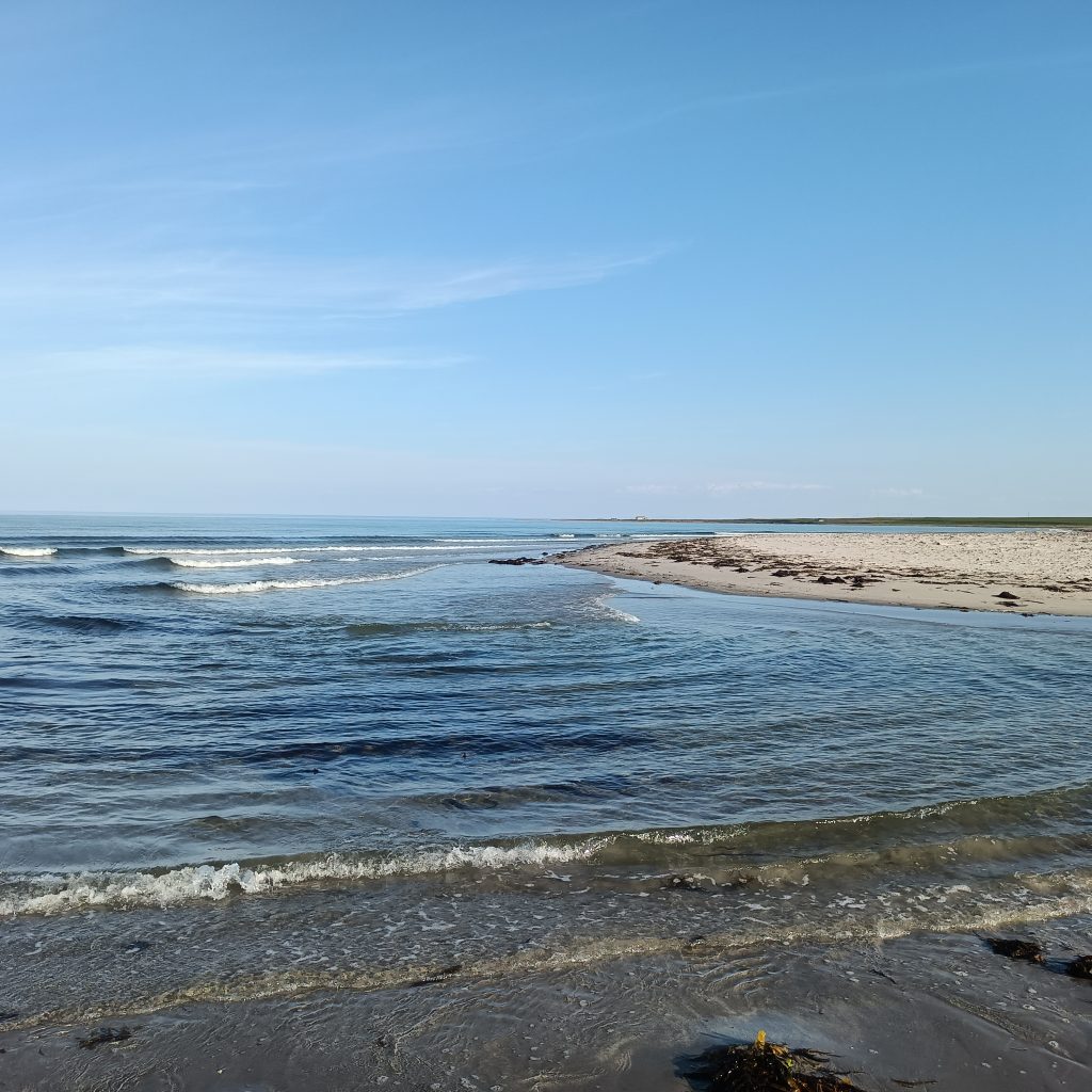 Kiesstrand und dahinter das Meer. Rechts ist Sandstrand.