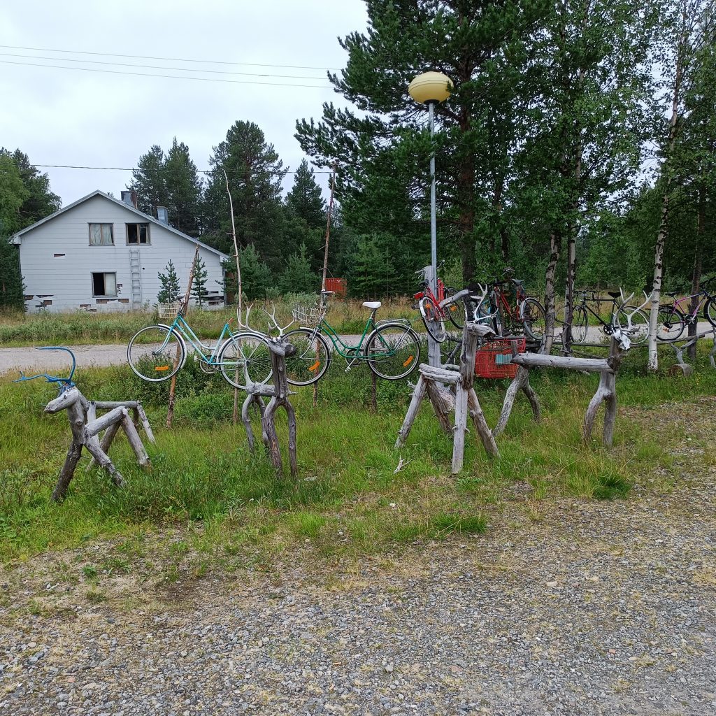Holzrentiere auf einer Wiese mit Weg und weißem Haus im Hintergrund
