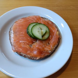 Teller auf braunen Untergrund. Darauf Brot mit Lachs und Gurke.