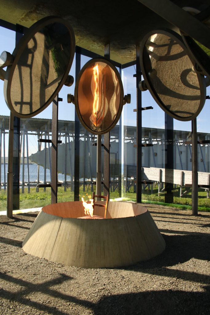 Brennder Stuhl im Betonkreis umgeben von drei Spiegel