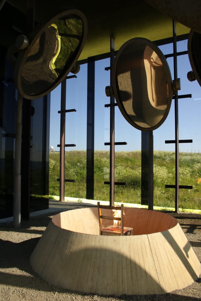 Brennder Stuhl im Betonkreis umgeben von drei Spiegel