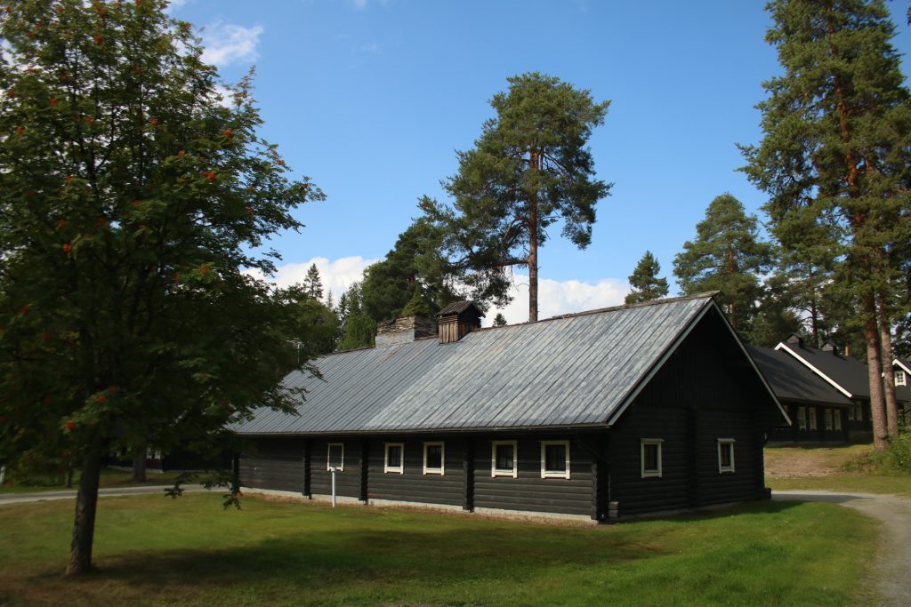 Eingeschoßiges Haus davor eine Wiese und Bäume links und dahinter