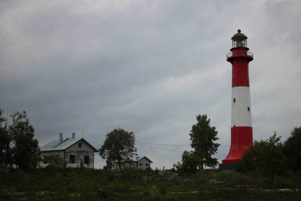 links Haus rechts Leuchtturm und Bäume