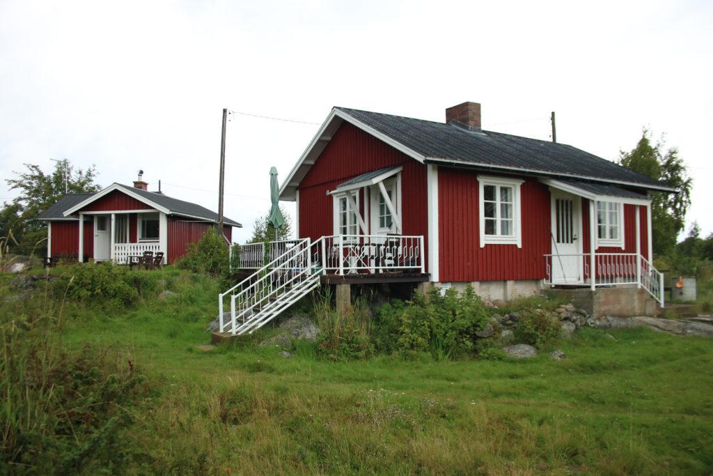 Wiese und reotes Holzhaus mit weißer Treppe